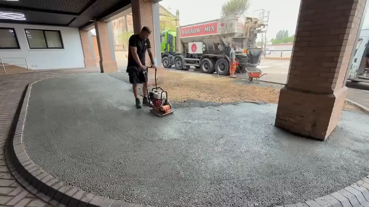 Worker compacting a no-fines concrete base at a Warrington office block with a Barrow Mix truck behind