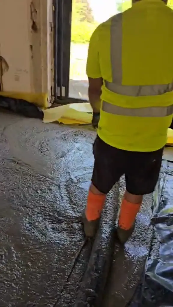 Worker levelling freshly pumped concrete on a house floor in Bolton