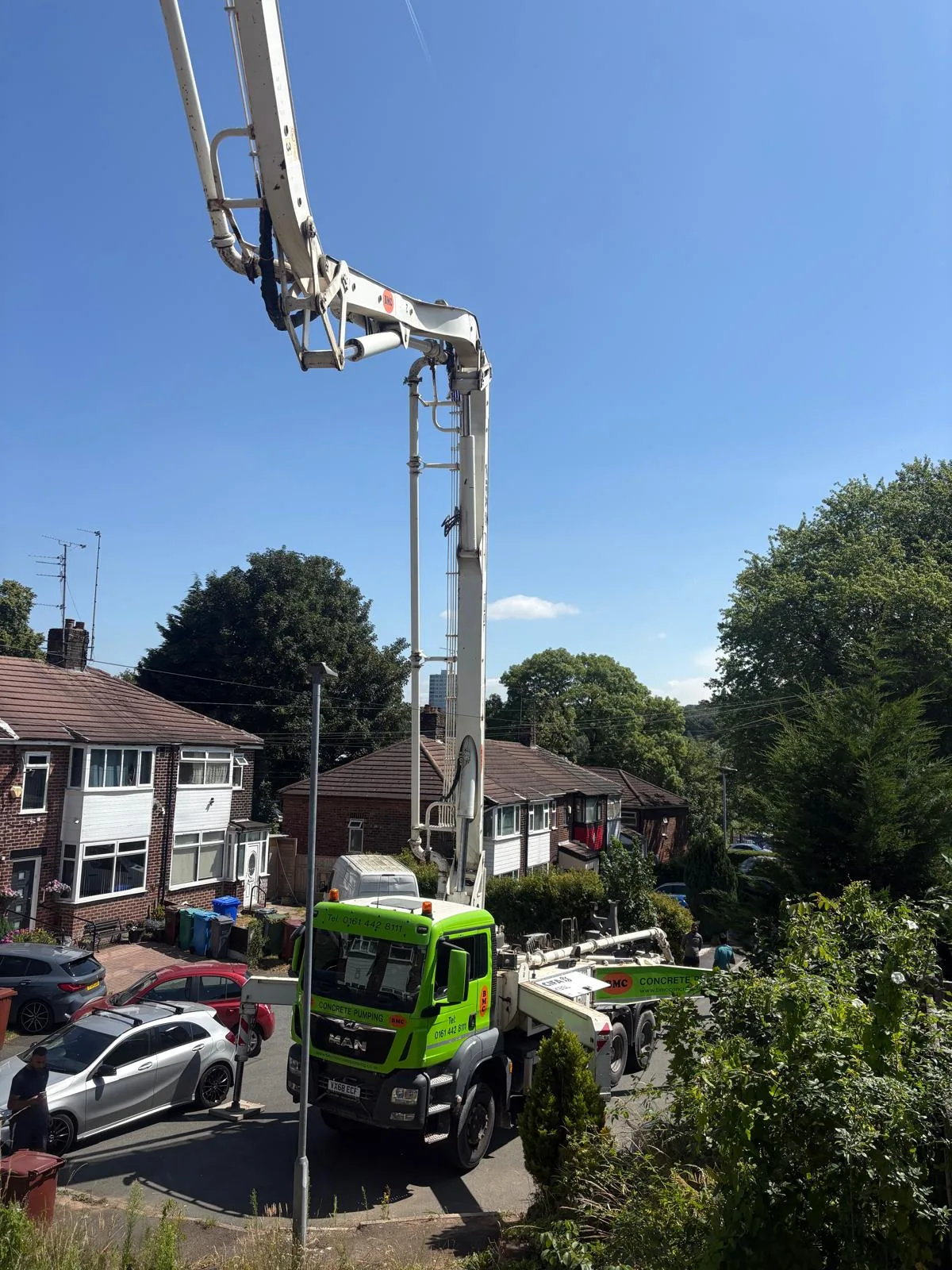 Barrow Mix boom pump reaching over a street to fill retaining-wall shuttering between two houses